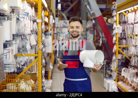 Happy Shop assistant qui travaille dans un magasin de détail de bricolage montrant le joint de tuyau en PVC et souriant Banque D'Images