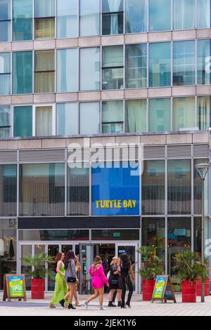 Des jeunes femmes qui marchent devant le bar-restaurant Turtle Bay Caribbean Eating & Drinking au Hub, Milton Keynes, Buckinghamshire, Royaume-Uni, en juin Banque D'Images