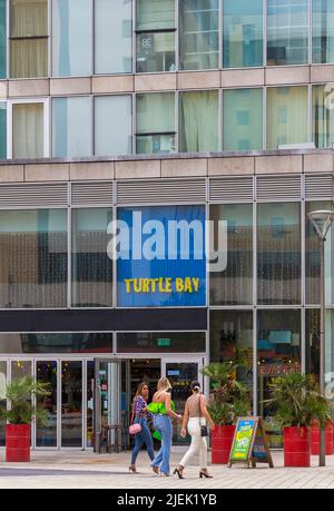 Des jeunes femmes qui marchent devant le bar-restaurant Turtle Bay Caribbean Eating & Drinking au Hub, Milton Keynes, Buckinghamshire, Royaume-Uni, en juin Banque D'Images