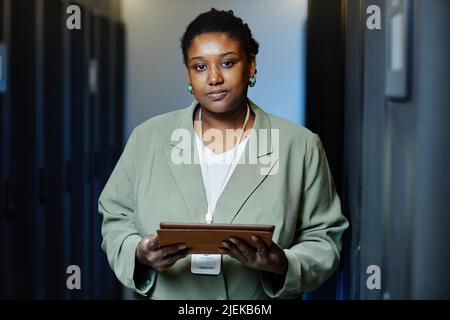 Portrait de face d'une femme afro-américaine souriante travaillant comme technicien INFORMATIQUE et utilisant une tablette dans une salle de serveurs Banque D'Images