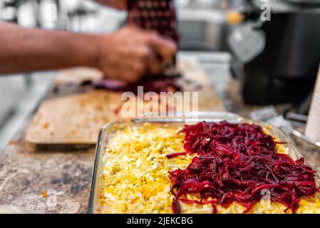 Gros plan de l'homme râpant des légumes en faisant un plat de salade russe traditionnel appelé shuba fait avec des betteraves superposées avec des pommes de terre, du hareng, des carottes et du mayonnaise Banque D'Images