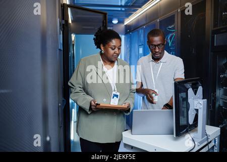 Portrait à la taille de deux jeunes noirs en tant qu'ingénieurs INFORMATIQUES utilisant un ordinateur portable dans une salle de serveurs lors de la configuration du réseau Banque D'Images