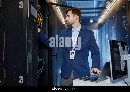 Portrait à la taille du jeune homme portant un blazer qui établit le réseau Internet dans la salle des serveurs Banque D'Images