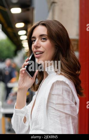 Femme souriante brune parlant sur smartphone dans la rue urbaine de Paris Banque D'Images