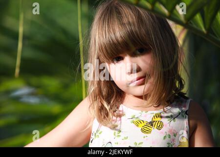 Petite fille européenne mignonne assise dans le jardin, portrait de plein air en gros plan Banque D'Images