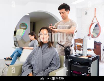 Jeune gars professionnel coiffeur coupe les cheveux de femme Banque D'Images