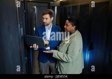 Vue en grand angle de deux personnes dans la salle des serveurs avec ordinateur portable et vérification de la sécurité des données Banque D'Images
