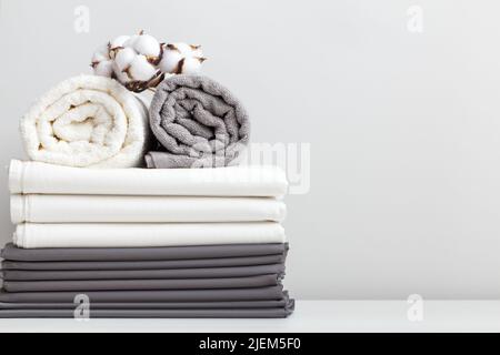 Linge de lit blanc gris, un drap et deux serviettes roulées sur la table. Banque D'Images