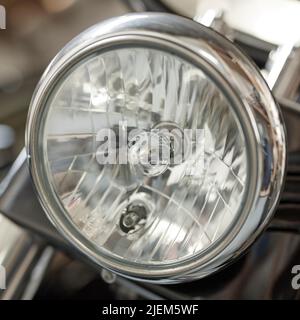 Gros plan d'un phare rond sur une moto classique. Une ampoule sur une moto rétro recouverte de chrome argenté bien entretenue. Véhicule à moteur Banque D'Images