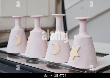 Rangée de quatre tasses en argile blanche ou en céramique avec des symboles d'étoile et de lune sur les côtés à l'envers sur le bord du conteneur dans l'atelier Banque D'Images