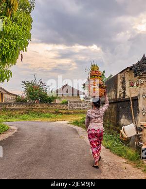 Femme marchant dans une rue portant des paniers avec des fruits sur sa tête. Banque D'Images