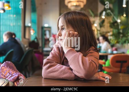 une jolie fille qui couve s'assoit à une table dans un café et regarde par la fenêtre Banque D'Images
