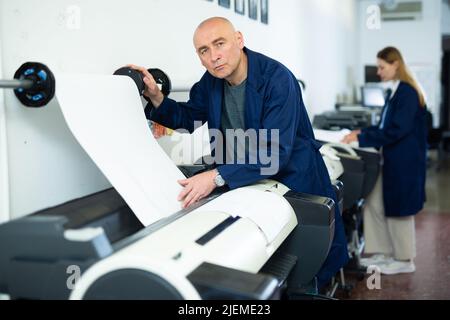 Homme travaillant dans un bureau d'impression, utilisant une imprimante Banque D'Images
