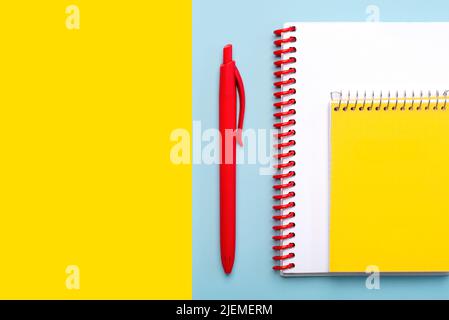 Vue de dessus du bloc-notes en spirale et du stylo rouge avec espace pour le texte sur fond bleu et jaune. Concept de retour à l'école Banque D'Images