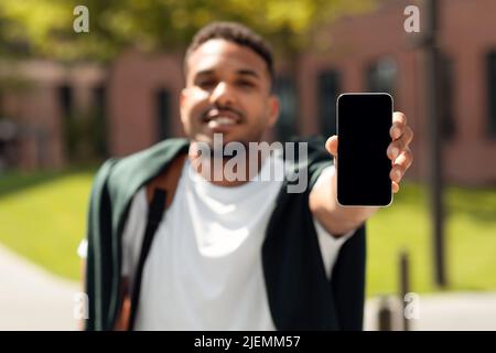 Homme noir élégant montrant le téléphone portable écran vide à l'extérieur, recommander une nouvelle application, marcher dans le parc, mockup Banque D'Images