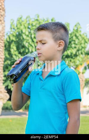 Un jeune garçon boit du soda dans une bouteille en plastique. Tir vertical. Banque D'Images