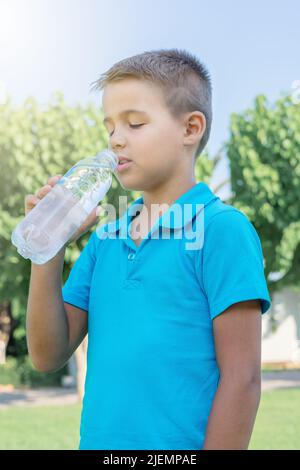 Un jeune garçon boit de l'eau dans une bouteille en plastique. Tir vertical. Banque D'Images