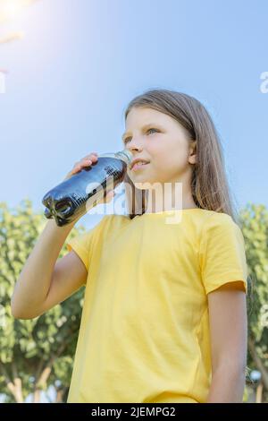 Une jeune fille boit du soda dans une bouteille en plastique. Tir vertical. Banque D'Images