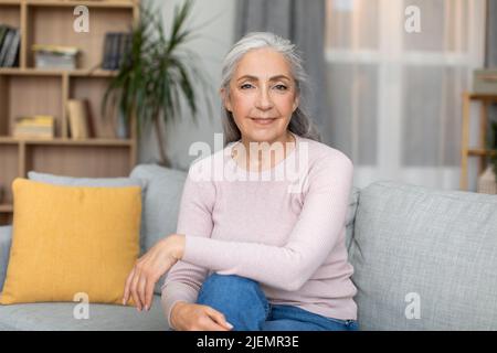 Joyeuse confiante calme jolie femme européenne senior avec cheveux gris, assis sur un canapé, aime le temps libre Banque D'Images