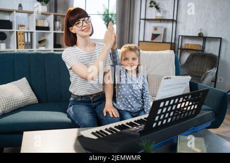 Je suis le gagnant. Mère et son agréable ont élué jolie petite fille donnant cinq élevé après avoir joué du piano à la salle de musique. Concept de leçon de musicien. Banque D'Images