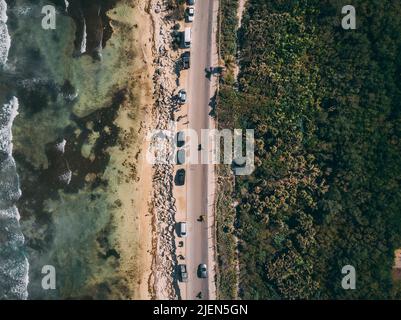 Vue aérienne en haut de la route de la plage de Tulum avec des voitures entre la plage de sable blanc des Caraïbes avec algues et forêt tropicale verte pendant un après-midi ensoleillé Banque D'Images