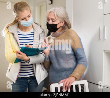 La femme mûre dans le masque de protection répond aux questions de l'intervieweur à la maison Banque D'Images