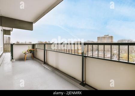 Grand balcon blanc avec garde-corps en métal noir, chaise en bois et plateau à fleurs Banque D'Images