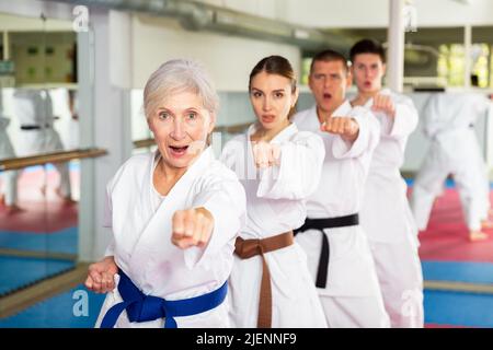 Femme âgée pratiquant des coups de poing pendant l'entraînement d'arts martiaux de groupe Banque D'Images