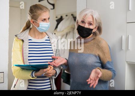 La femme mûre dans le masque de protection répond aux questions de l'intervieweur à la maison Banque D'Images