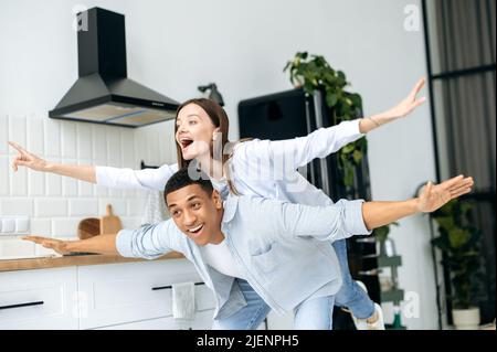 Couple heureux multiracial dans l'amour, fille caucasienne et type latino, vêtu d'un vêtement moderne décontracté, s'amuser ensemble à la maison dans la cuisine, rire, profiter du week-end, éprouvant des émotions positives Banque D'Images