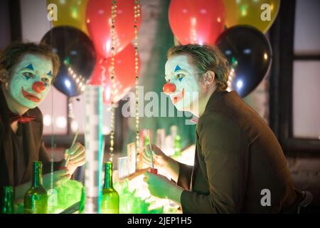 Clown concept - un homme assis dans le dressing et peignant un sourire rouge sur son visage Banque D'Images
