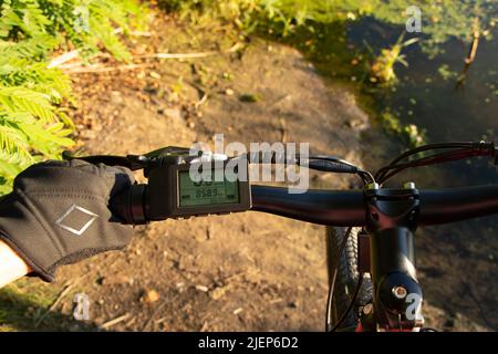 une main femelle dans un gant noir tient le volant d'un e-bike au soleil dans le parc, conduisant un e-bike, se reposant sur un vélo Banque D'Images