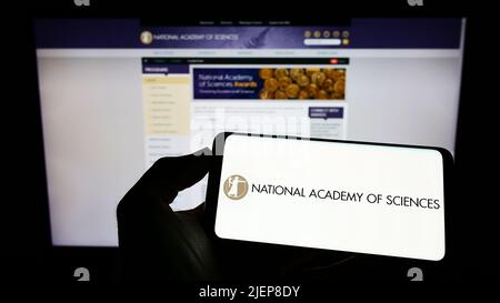 Personne tenant un téléphone portable avec le logo de l'Académie nationale des sciences (NAS) à l'écran en face de la page Web. Mise au point sur l'affichage du téléphone. Banque D'Images
