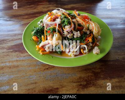 Cuisine thaïlandaise salade épicée à la feuille de Seablite bouillie ( Suaeda maritima ) avec calmar et crevettes dans un plat vert sur une table en bois brun, fruits de mer en Thaïlande Banque D'Images