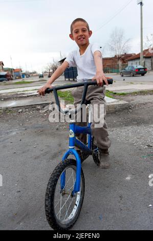 Sofia, Bulgarie. Un jeune garçon ROM pré-adolescent montrant son vélo et son vélo tout en jouant à l'intérieur du Ghetto Roma Hristo Botev. Les écoles étant souvent hors de question pour les Roms, il a amplement le temps de jouer et de se faire instruire par les coutumes de la rue. Banque D'Images