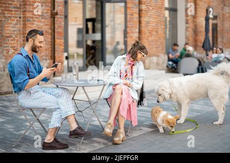 Couple assis au café pendant que les chiens jouent autour Banque D'Images