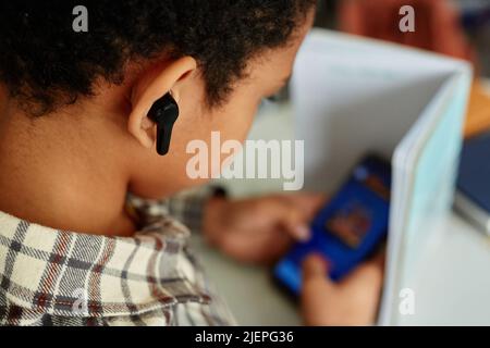 Gros plan sur l'écoute de la musique d'un enfant noir pendant la classe et le masquage du téléphone et de l'espace de copie Banque D'Images