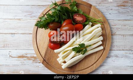 Fromage à cordes ou fouet au fromage - en-cas salé avec tomates cerises et herbes sur la planche à découper. Fromage turc Banque D'Images