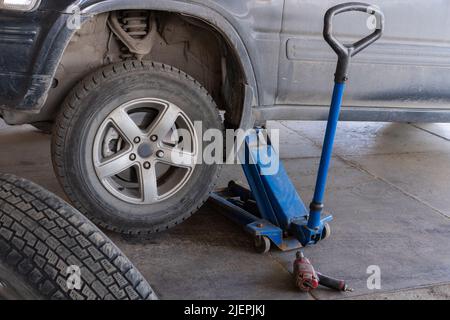 Soulever une voiture pour changer un pneu après une crevaison avec le cric inséré sous la carrosserie en soulevant le véhicule. Remplacement des roues d'une voiture. Banque D'Images