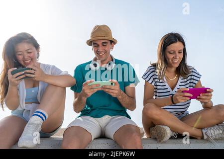 Groupe multiculturel de jeunes amis branchés qui s'amusent sur les smartphones et les réseaux sociaux. Jeux mobiles. Banque D'Images