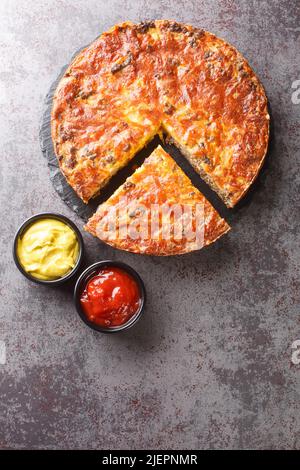 Tarte savoureuse au cheeseburger de style sudiste avec fromage cheddar au bœuf haché et oignon en gros plan sur une plaque d'ardoise sur la table. Vue verticale du dessus Banque D'Images