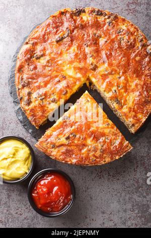 Tarte au cheeseburger avec fromage cheddar de bœuf haché et gros-plan d'oignon sur un plateau d'ardoise sur la table. Vue verticale du dessus Banque D'Images