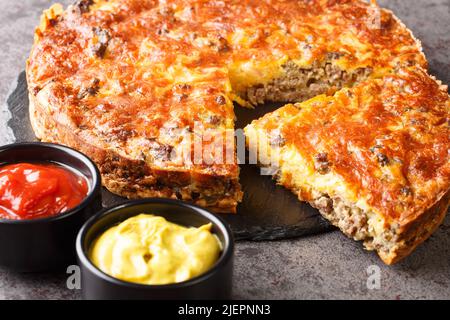 Tarte au cheeseburger au bœuf servie avec des sauces en gros plan sur un tableau d'ardoise sur la table. Horizontale Banque D'Images