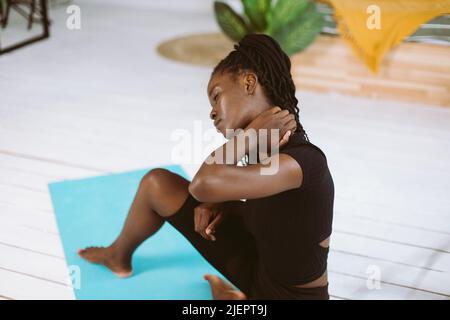Femme multiraciale à peau foncée avec des dreadlocks s'étirant, faisant des exercices de yoga sur le tapis en salle de gym. Appliquer de la crème sur un col rigide Banque D'Images
