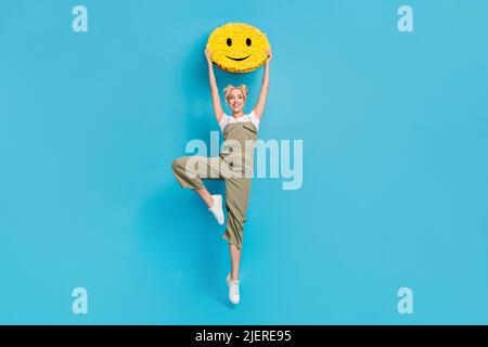 Photo pleine grandeur de belle blonde dame saut avec pinata porter t-shirt général chaussures isolées sur fond bleu Banque D'Images