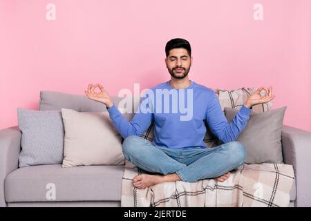 Photo de l'homme arabe paisible rêveur porter chemise à manches longues canapé s'entraînant yoga isolé couleur rose fond Banque D'Images