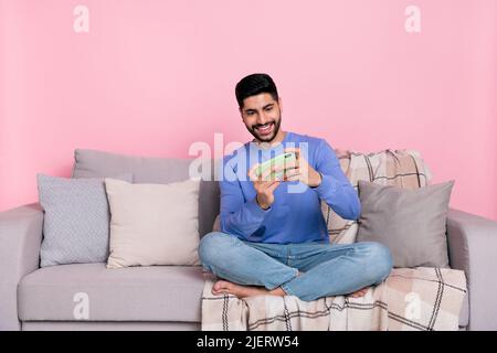 Photo de funky positif arabian man porter chemise à manches longues salon canapé jouer moderne gadget vide espace isolé couleur rose arrière-plan Banque D'Images