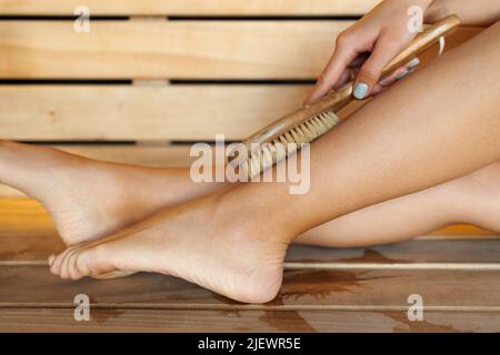 Gros plan des jambes de la femme effectuant un massage avec une brosse en bois sèche pendant les soins du spa Banque D'Images