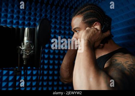 Gros plan du beau jeune chanteur noir debout devant la chanson de chant du microphone dans le studio d'enregistrement Banque D'Images
