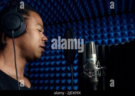 Gros plan du beau jeune chanteur noir debout devant la chanson de chant du microphone dans le studio d'enregistrement Banque D'Images
